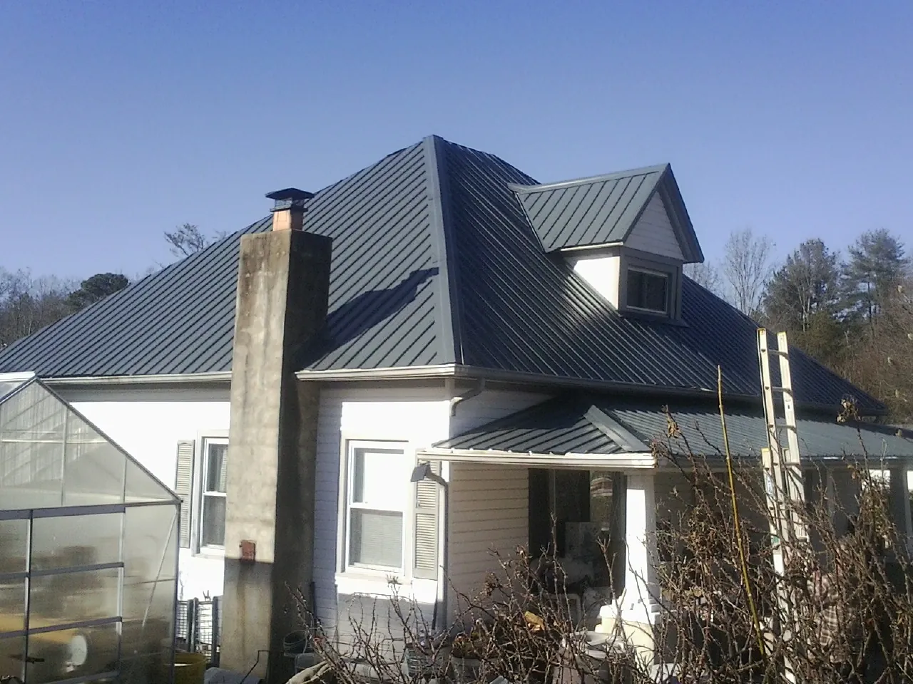 Dark blue standing seam metal roof on a white farmhouse with dormer — Slate & Tile Roof Repair by Roofing Brothers in Locust Gap