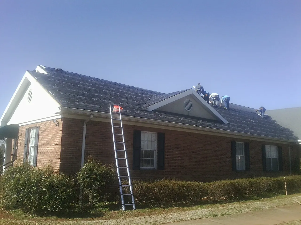 Crew tearing shingles off a brick ranch roof with a ladder set — Emergency Roof Repair work by our crew in Locust Gap