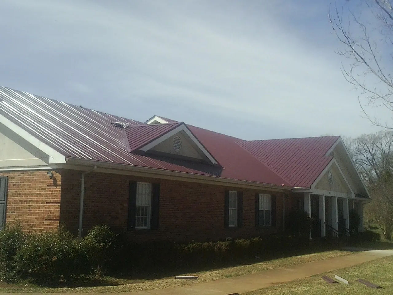 Red metal roof with gabled entries on a long brick building, from a Hail Damage Roof Repair job in Locust Gap