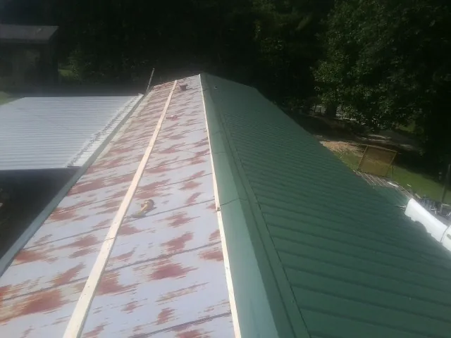 Old rusted panels beside newly installed green metal roofing — Wind Damage Roof Repair by Roofing Brothers in Locust Gap