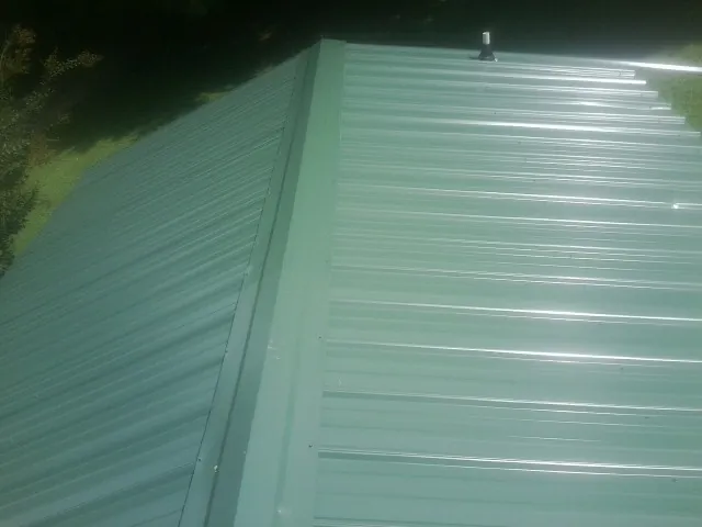 New green metal panels meeting at the ridge of a roof — Flat Roof Repair work by our crew in Locust Gap