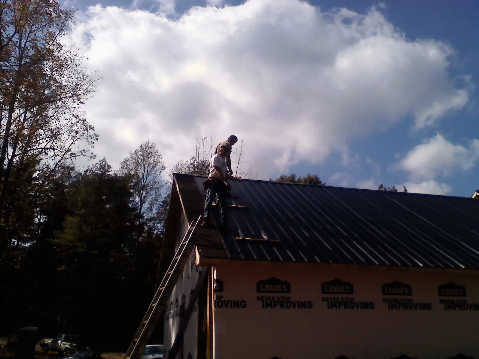Roofer fastening dark metal panels high against a cloudy sky, from a Roof Inspection job in Locust Gap