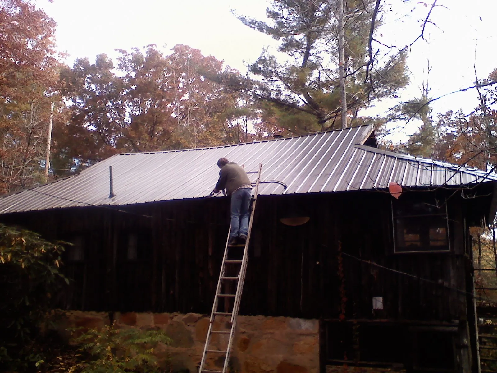 Roofer on a ladder working along the edge of a cabin metal roof in Locust Gap