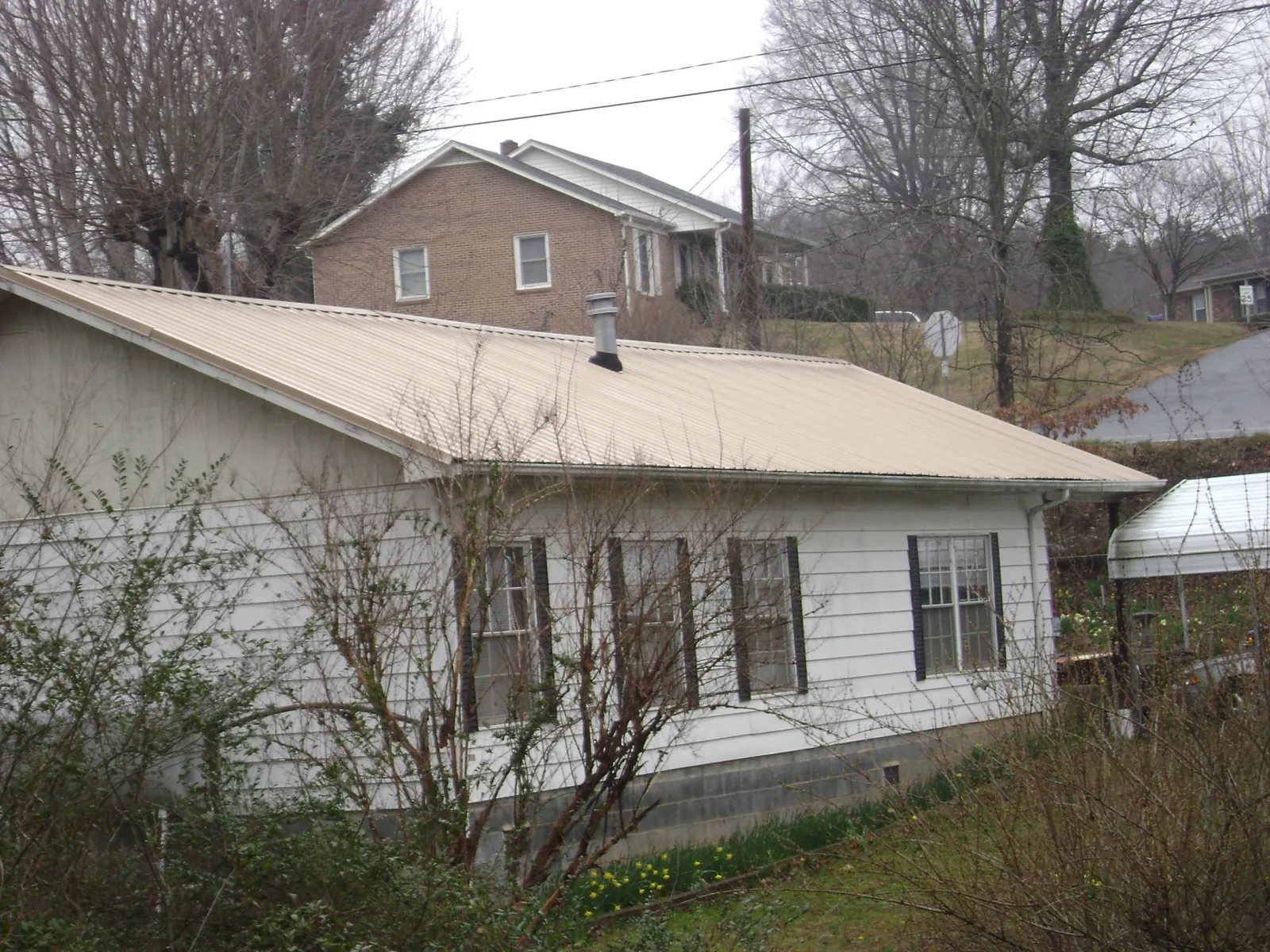 Tan metal roof on a white sided house set into a hillside — Commercial Roofing by Roofing Brothers in Locust Gap