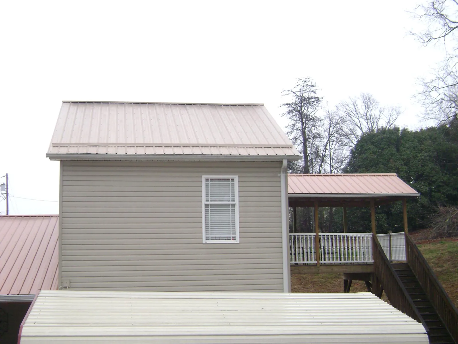 Tan metal roofs on a two story addition and attached porch, from a Roof Replacement job in Locust Gap